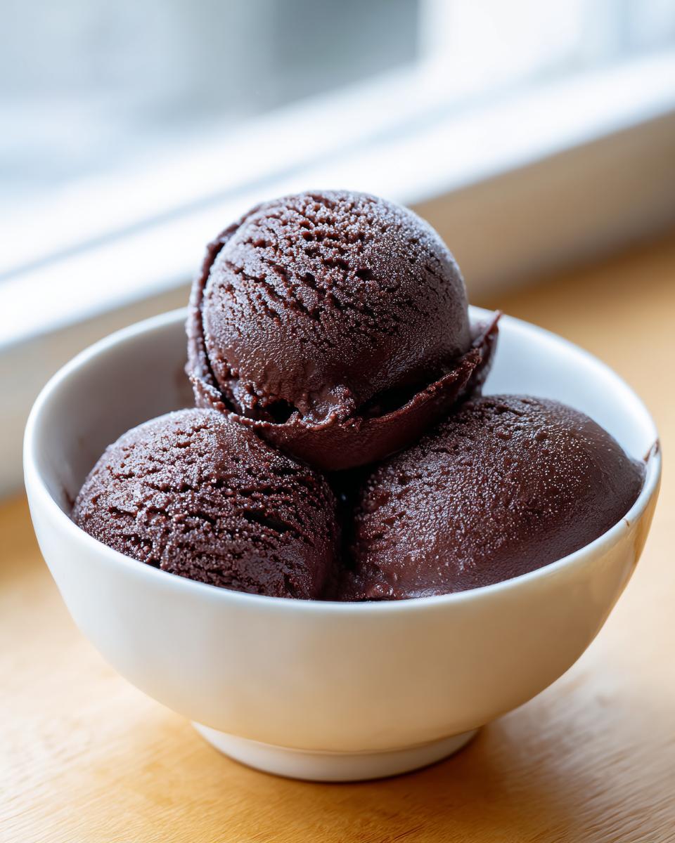Three perfectly scooped portions of rich, dark chocolate sorbet served in a white bowl.