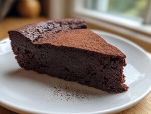 A rich, dense slice of flourless chocolate torte dusted with cocoa powder, served on a white plate.