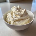 A close-up of fluffy, whipped Cottage cheese vanilla mousse served in a small white bowl on a light countertop.