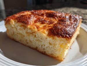 A thick, fluffy slice of sheet pancakes with a golden-brown, slightly caramelized top, served on a white plate.