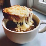 Close-up of French onion soup with a thick layer of melted, stretchy cheese dripping off a toasted bread crouton.