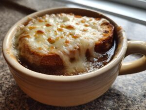 Close-up of a bowl of rich French onion soup topped with a thick crouton and bubbly, melted Gruyère cheese.