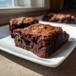Close-up of a rich, dark, fudgy Cottage Cheese Brownie slice with a crackly top, served on a white plate.