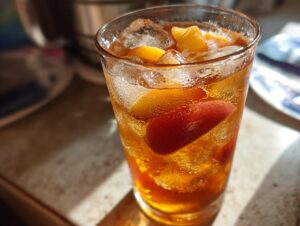 Close-up of a sweating glass filled with cold Peach iced tea, ice cubes, and fresh peach slices.