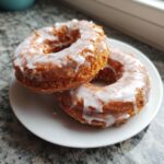 Two delicious Old fashioned cake donut treats stacked slightly on a white plate, covered in thick white glaze.