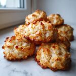 A close-up stack of freshly baked, golden brown almond macaroon cookies resting on a white marble surface.