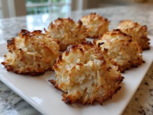 Close-up of several perfectly baked almond macaroon treats with toasted edges, arranged on a rectangular white serving dish.