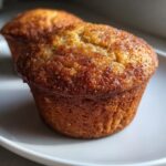 Close-up of a perfectly baked applesauce muffin with a golden-brown, sugary, cinnamon-dusted top.