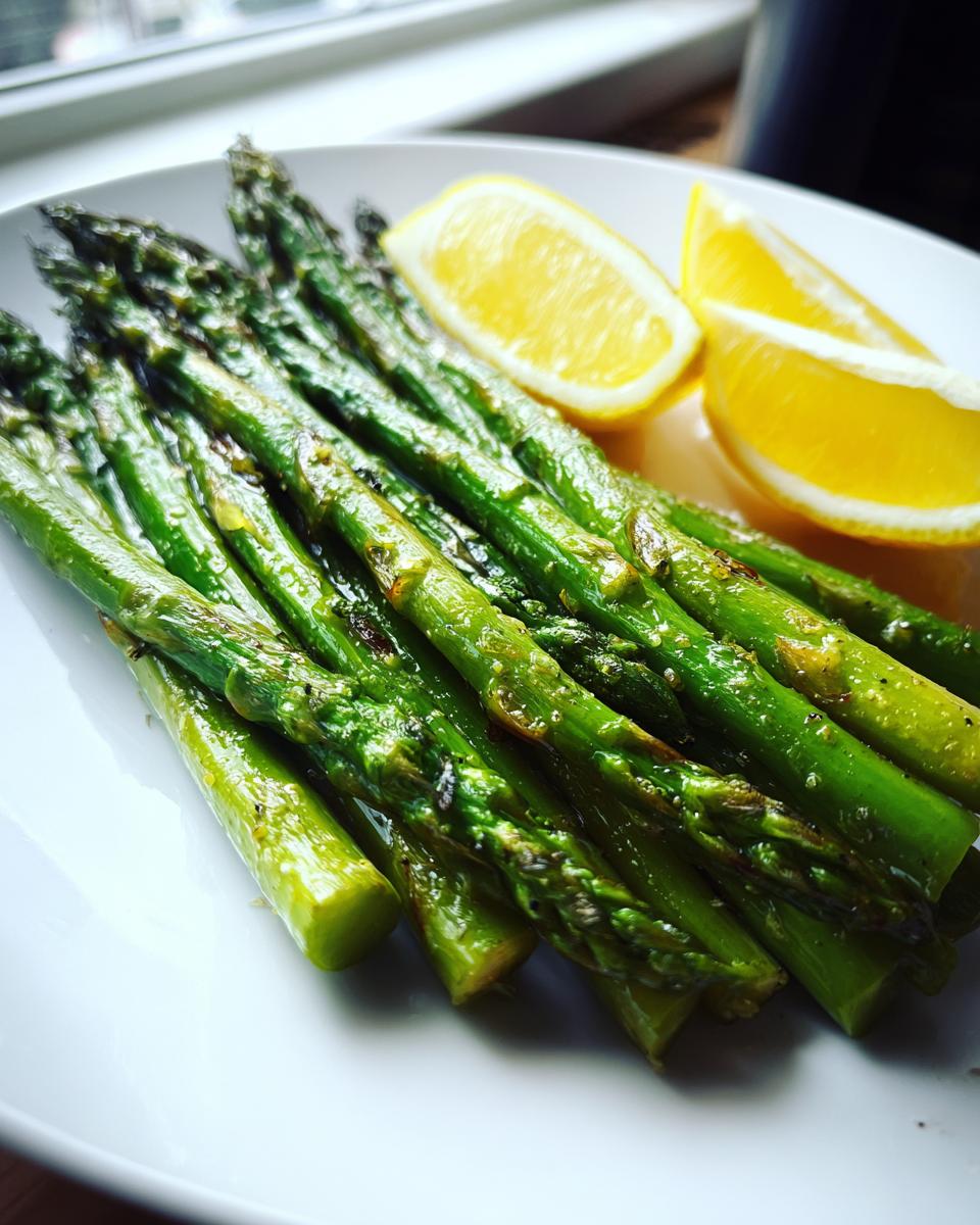 A close-up of bright green grilled asparagus with lemon slices served on a white plate.