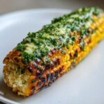 Close-up of perfectly grilled corn with charred kernels topped with melted butter and fresh green herbs.