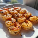 Close-up of perfectly cooked, seasoned grilled shrimp skewer pieces resting on a bright white plate.