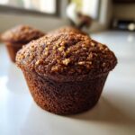 A close-up, appetizing photo of a rich, dark Hazelnut espresso muffin topped with crunchy nuts.