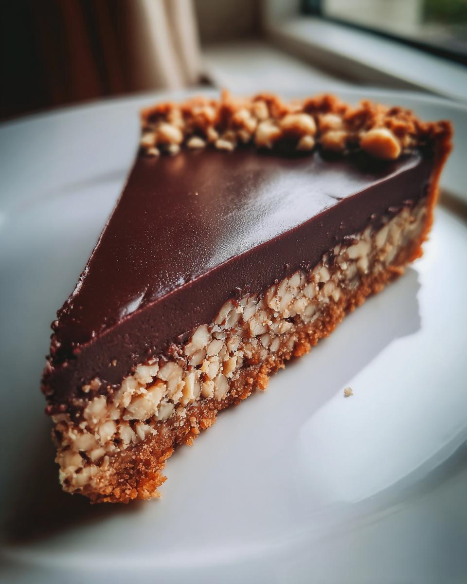 A perfect slice of Hazelnut praline tart featuring a crunchy nut layer and a smooth chocolate ganache topping.