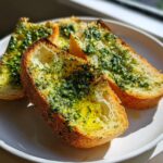 Three golden-brown slices of toasted baguette generously topped with vibrant green herb butter, served on a white plate.