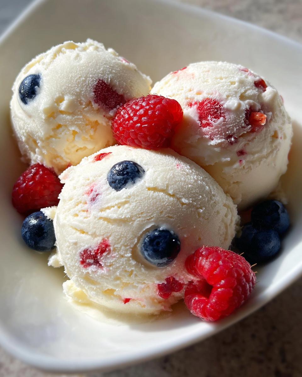 Three scoops of creamy Homemade frozen yogurt studded with blueberries and raspberries in a white bowl.