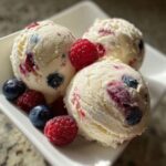 Three scoops of creamy homemade frozen yogurt swirled with blueberries and raspberries, garnished with fresh berries.