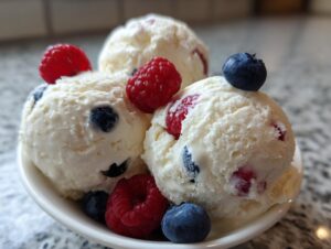 Three scoops of creamy homemade frozen yogurt mixed with raspberries and blueberries in a white bowl.