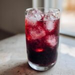 Close-up of a tall glass filled with iced Blackberry sage tea, showing deep red liquid and condensation.