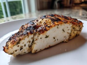 Close-up of a perfectly cooked Lemon herb grilled chicken breast, showing juicy white meat and herb crust.