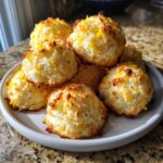 A pile of freshly baked, golden-brown Lemon Zest Macaroon cookies topped with bright yellow zest.