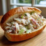 A close-up of a perfectly filled Maine lobster roll in a toasted bun, showcasing creamy lobster salad with celery.