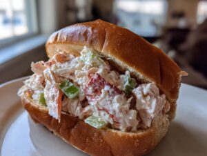 A close-up of an Ultimate 4-Ingredient Maine lobster roll, featuring creamy lobster salad with celery in a toasted split-top bun.