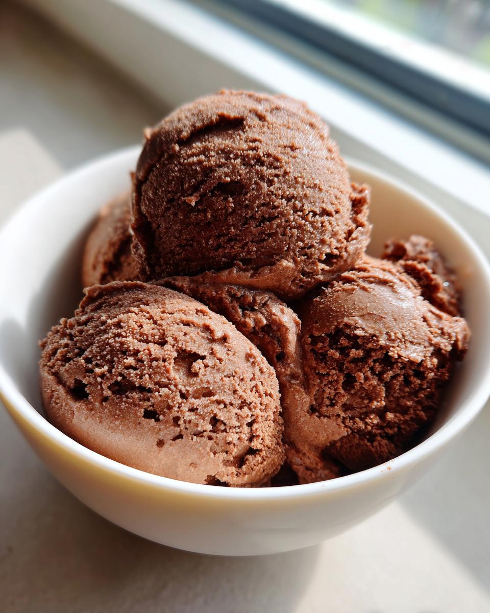 Close-up of several scoops of rich, dark brown Mexican chocolate ice cream served in a white bowl near a window.