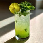 A tall, sweating glass filled with bright green Mint limeade, crushed ice, muddled mint, and garnished with a lime wheel and fresh mint sprig.