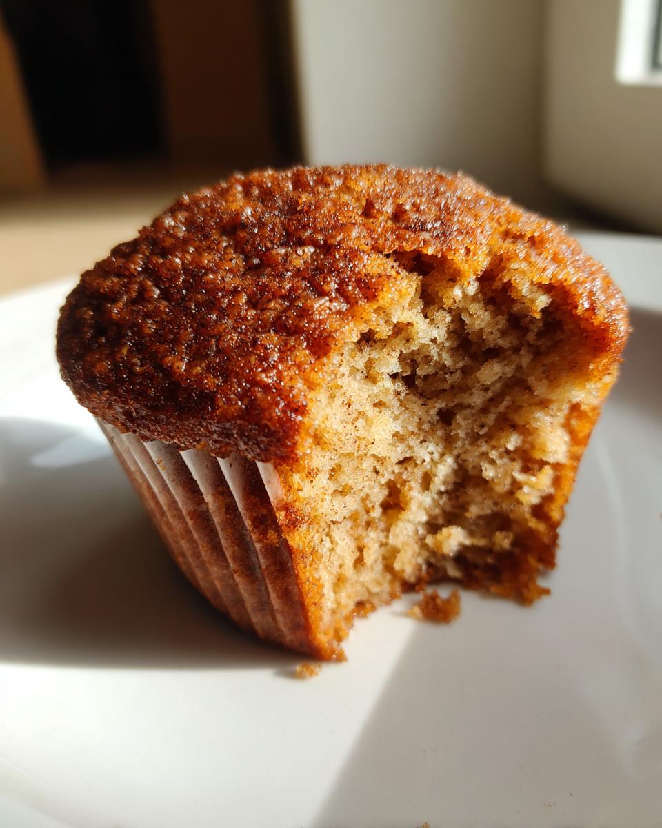Close-up of a moist, golden brown applesauce muffin with a bite missing, showing the soft interior texture.
