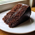 A close-up of a single slice of Moist devil's food cake on a white plate, showing its dark, rich crumb.