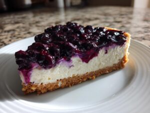 A close-up of a slice of no-bake blueberry cheesecake showing the graham cracker crust, creamy filling, and rich blueberry topping.