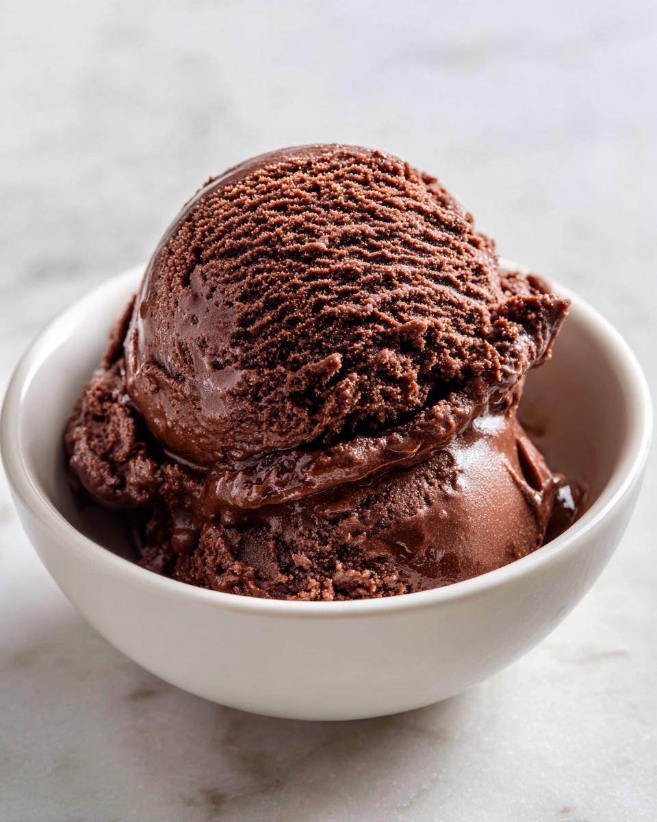 Two rich scoops of dark No churn chocolate ice cream served in a small white bowl.