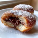 Close-up of a warm Nutella filled donut, cut in half, showing molten chocolate oozing out, dusted with sugar.