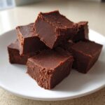 A stack of rich, dark squares of Old fashioned chocolate fudge piled on a white plate.