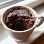 Close-up of a rich, dark brown Protein chocolate mug cake baked inside a light-colored mug.