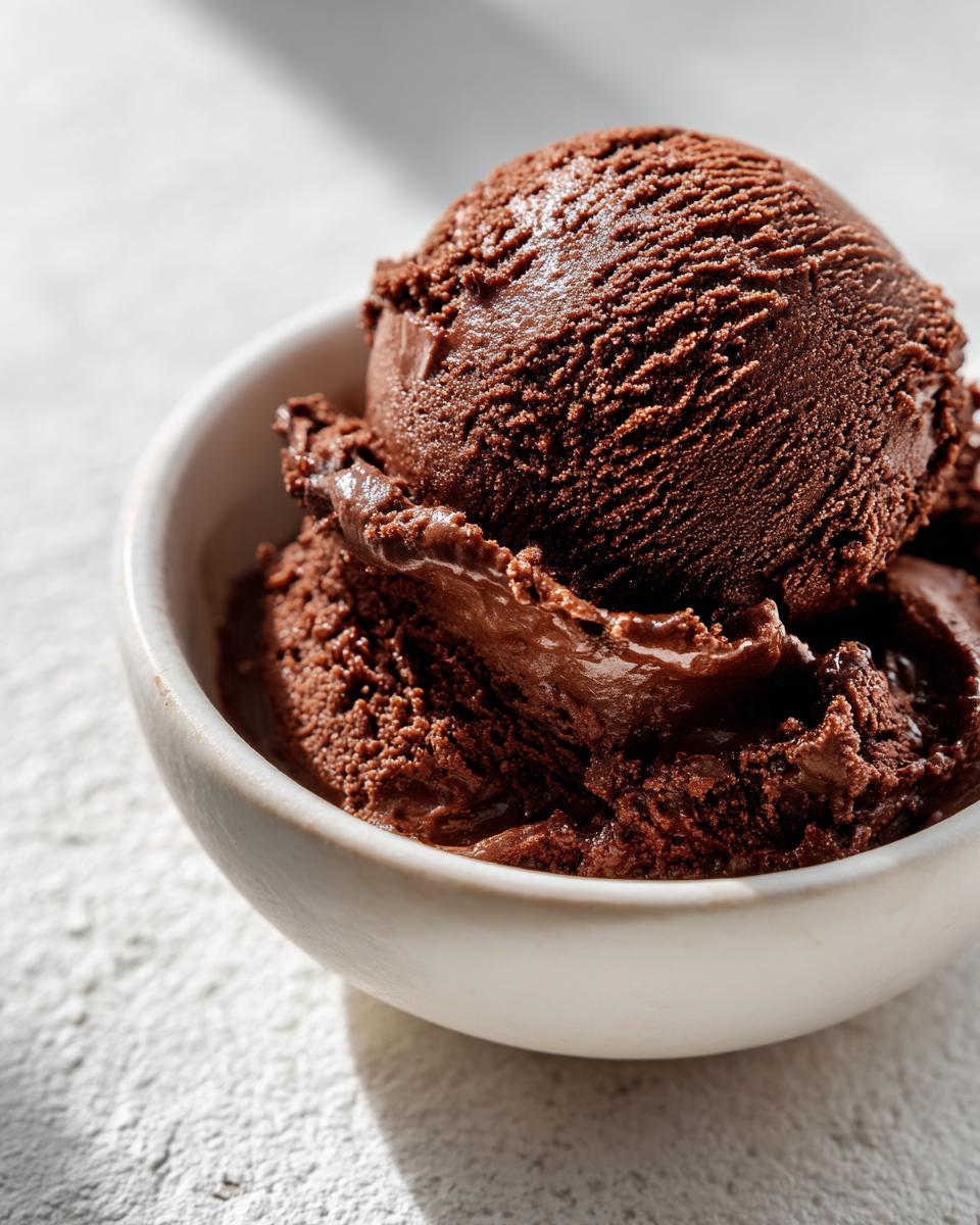 Close-up of a rich, dark scoop of homemade chocolate gelato in a small white bowl.
