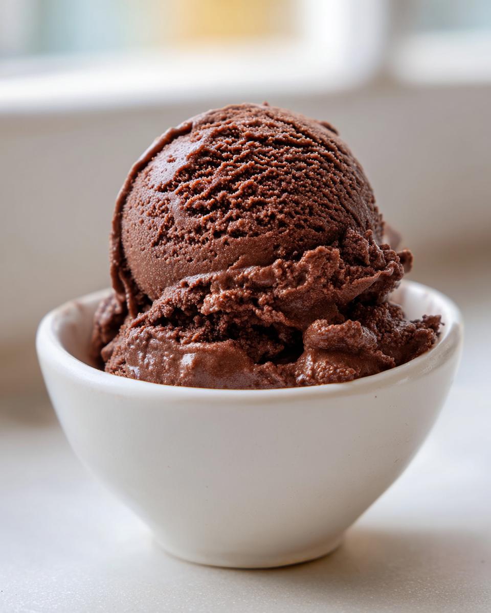 Close-up of a perfectly scooped portion of rich, dark chocolate gelato served in a small white bowl.