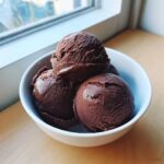 Three scoops of rich, dark chocolate sorbet piled high in a small white bowl on a wooden surface.