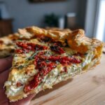 Close-up of a thick slice of savory sun-dried tomato galette showing flaky crust and creamy filling.