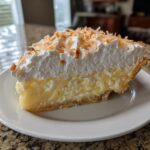 A generous slice of creamy Coconut cream pie topped with whipped cream and toasted coconut flakes.