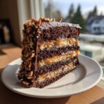 A tall slice of German chocolate cake with four dark chocolate layers and coconut-pecan filling, sitting on a white plate.