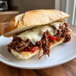 A delicious sandwich filled with shredded Slow Cooker Italian Beef, peppers, and melted provolone cheese on a hoagie roll.