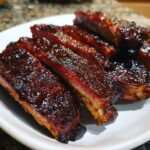 Close-up of perfectly cooked, glazed Smoky BBQ ribs sliced and served on a white plate.