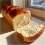 A freshly baked loaf of soft Honey milk bread with a single slice cut, showing the fluffy white interior.