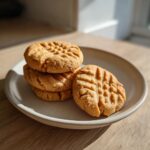 A stack of four and one loose Soft peanut butter cookie with classic crosshatch marks on a light ceramic plate.
