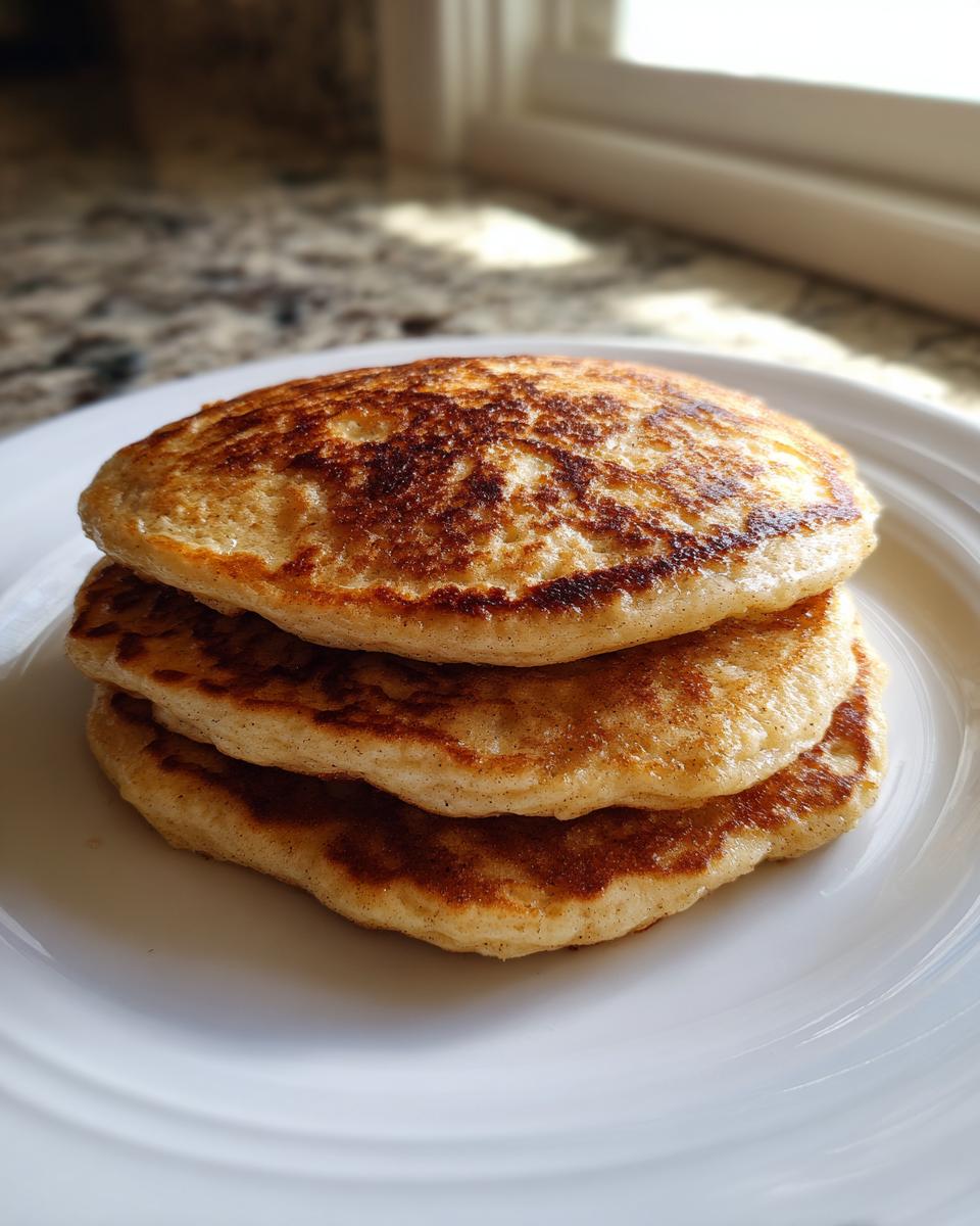 A stack of three perfectly golden brown Applesauce pancake served on a white plate near a window.