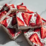 Close-up of several square cuts of strawberry froyo bark topped with fresh strawberries and chia seeds.