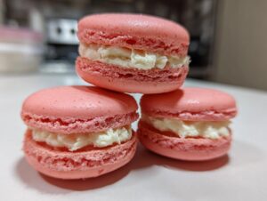 Three perfectly formed pink strawberry macaroon cookies stacked, showing creamy white filling.
