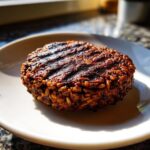 A close-up of a perfectly grilled, sturdy black bean burger patty showing distinct grill marks on a white plate.