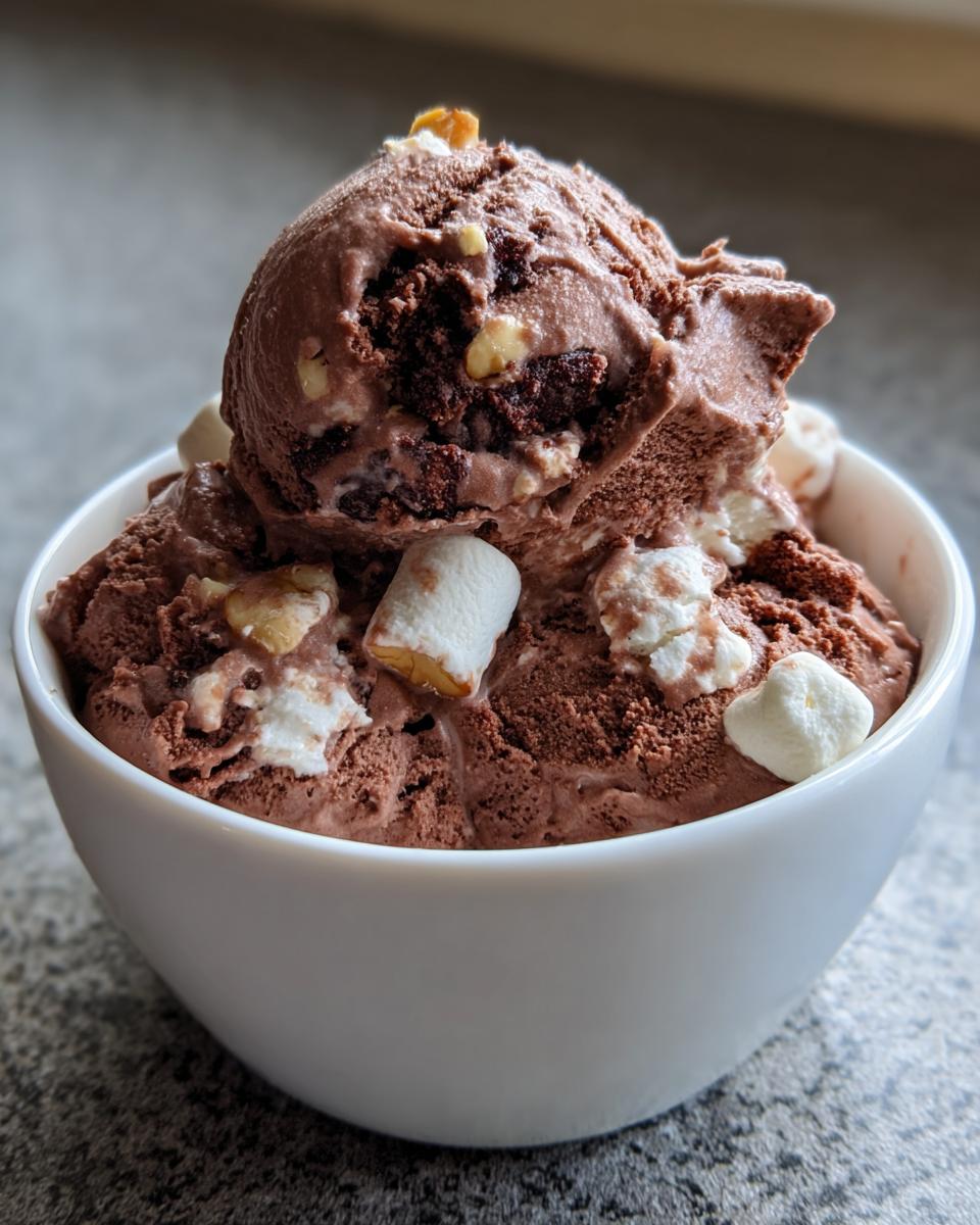 A thick scoop of rich chocolate Rocky Road ice cream loaded with marshmallows and nuts in a white bowl.